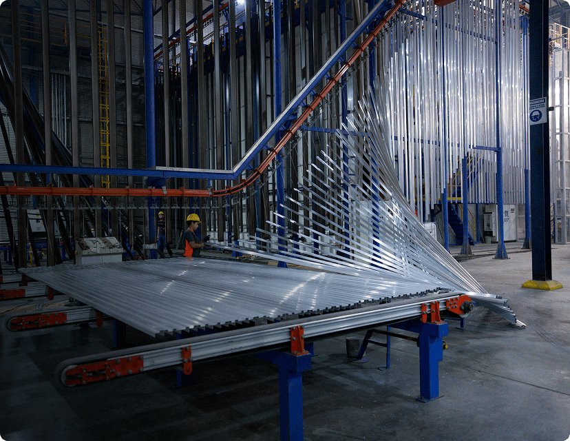 Aluminum profiles are being sorted on a conveyor belt within a large industrial facility.