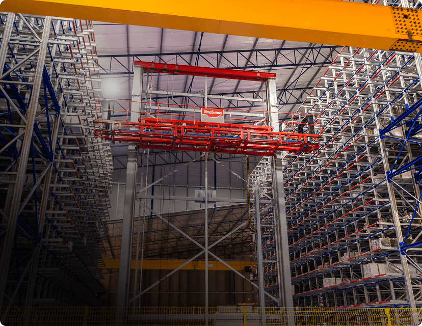 Automated crane moves goods in a high-bay warehouse. Dino-Siege is visible on the crane.